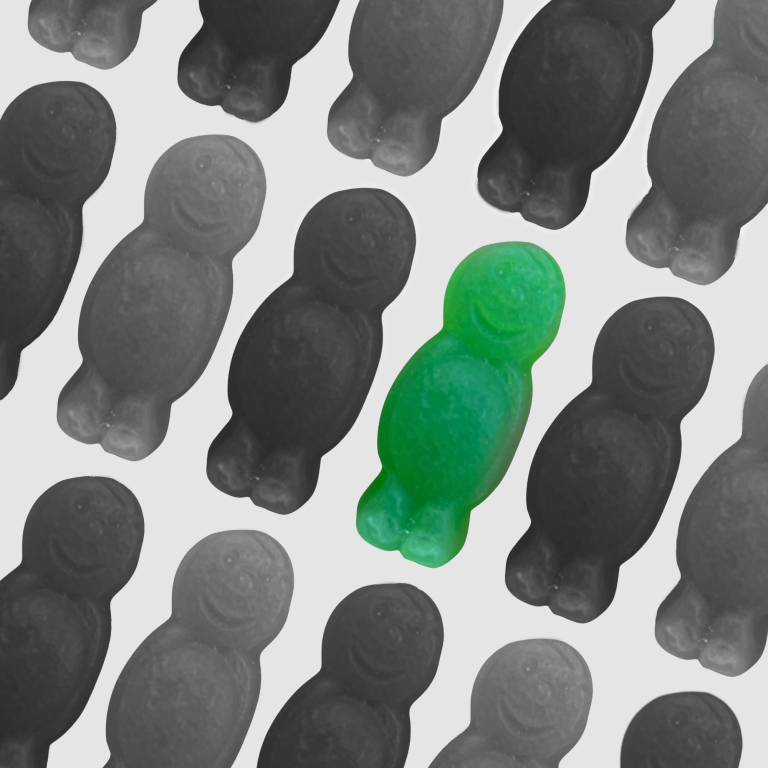 A green Jelly Baby within a group of black and white Jelly Babies.